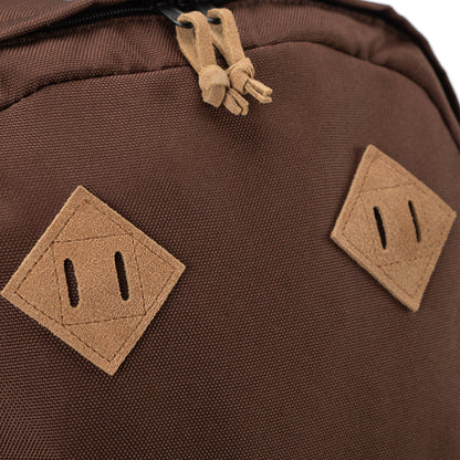 Close-up of brown backpack showing suede zipper pulls and two tan suede lash tabs stitched onto the front panel.